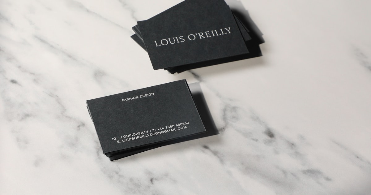 Two printed business cards resting on a marble countertop showing trimmed edges and card stock